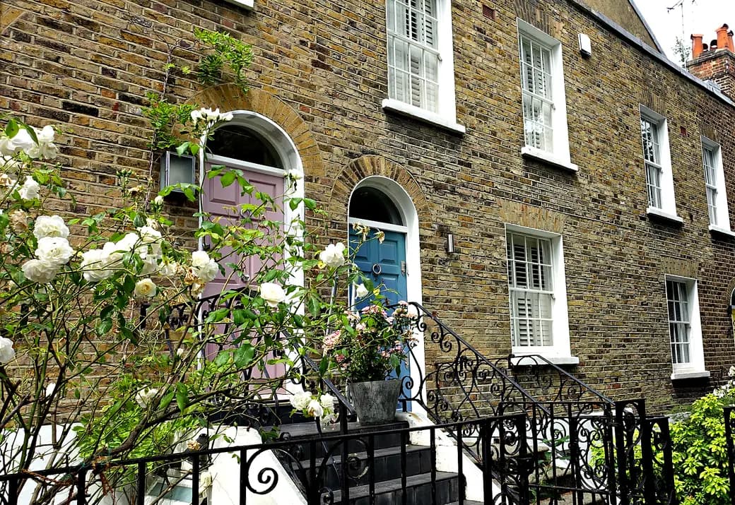 A London terrace of stock brick, arched doorways with painted front doors, steps and iron railings.